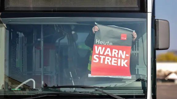 Ein Mitarbeiter befestigt ein Warnstreik-Plakat in einem Bus an der Frontscheibe. | picture alliance/dpa , Jan Woitas Ein Mitarbeiter befestigt ein Warnstreik-Plakat in einem Bus an der Frontscheibe.