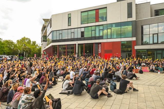 Student*innen halten eine Vollversammlung vor dem Uni-Gebäude ab.