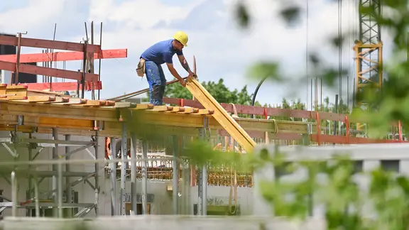 Ein Bauarbeiter nimmt auf einer Baustelle einen Balken entgegen. (Symbolfoto) | picture alliance / Sven Simon, Frank Hoermann/SVEN SIMON Ein Bauarbeiter nimmt auf einer Baustelle einen Balken entgegen. (Symbolfoto)