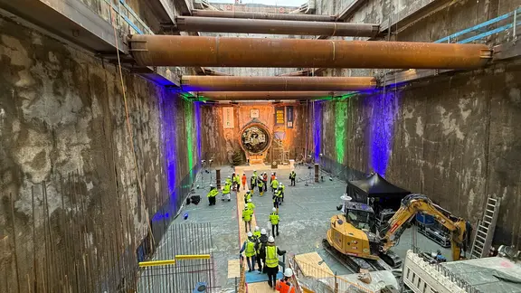 Ein Tunnel mit Rohren, Bauarbeitern und einem Bagger.