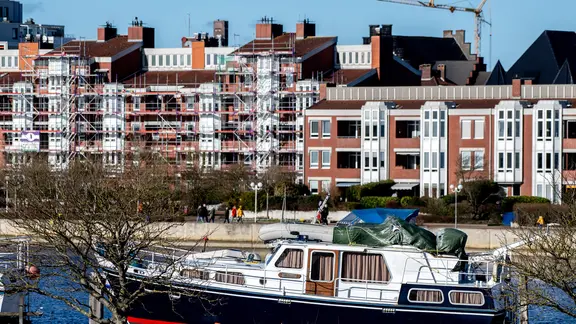 Ein Motorboot liegt am Südstrand in einem Winterlager, während im Hintergrund die Wohnhäuser am Bontekai in Wilhelmshaven zu erkennen sind.