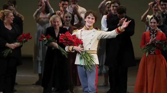 Tänzer Callum Linnane auf der Bühne. | Lucas Dawson Tänzer Callum Linnane steht mit einem Strauß Blumen im Arm auf einer Bühne und lächelt.