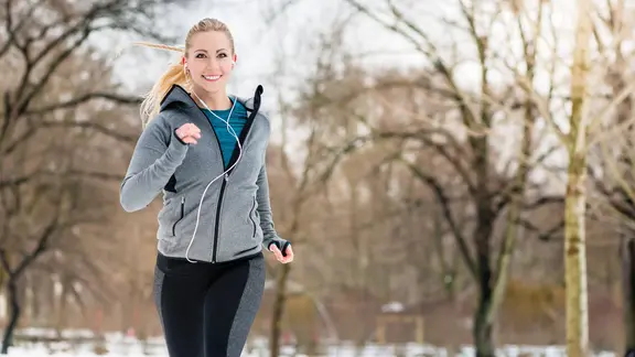 Eine junge Frau joggt durch eine Winterlandschaft. | IMAGO / YAY Images, IMAGO / YAY Images Eine junge Frau joggt durch eine Winterlandschaft.