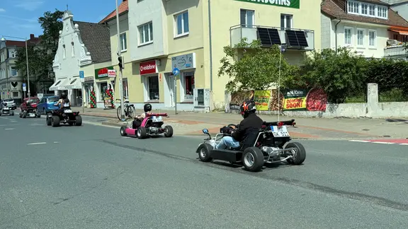 Auf der Straße sind die Karts deutlich kleiner und niedriger als die Autos um sie herum. | NDR, Niels Kristoph Mehrere Go-Karts fahren auf der Straße.