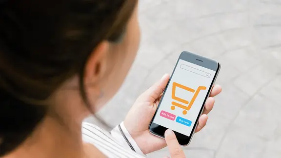 Eine Frau schaut auf ihr Smartphone mit dem Bild eines Einkaufswagens. | Colourbox Eine Frau schaut auf ihr Smartphone mit dem Bild eines Einkaufswagens.