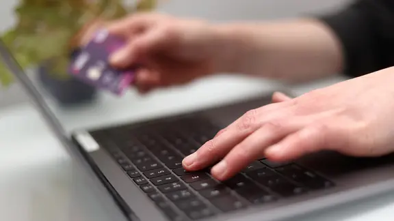 Eine Person tippt auf einer Computertastatur und hält eine Bankkarte in der anderen Hand. | picture alliance / empics, Tim Goode Eine Person tippt auf einer Computertastatur und hält eine Bankkarte in der anderen Hand.