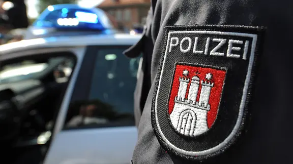 Ein Beamter der Polizei Hamburg vor einem Streifenwagen.
