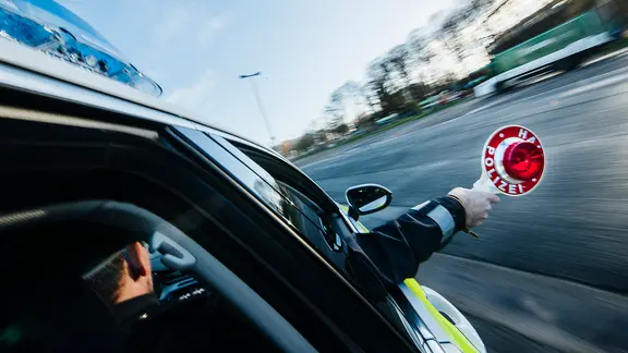 Ein Polizist hält eine rote Polizeikelle aus dem Beifahrerfenster eines Streifenwagens heraus.