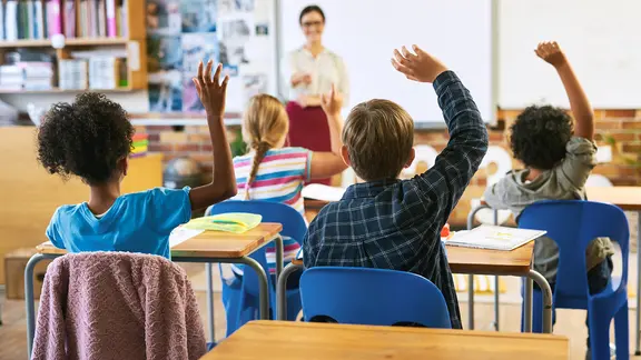 Kinder sitzen in einem Klassenraum und melden sich. | AdobeStock/HockleyMedia_peopleimages.com Kinder sitzen in einem Klassenraum und melden sich.