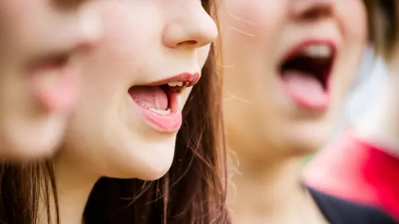 Das Festival findet unter dem Motto "Wer singt, blüht auf!" statt. | Wiebke Ostermeier Drei Frauen haben ihre Münder zum Singen geöffnet.