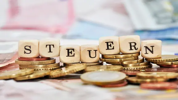 Würfel mit der Aufschrift "Steuern" liegen auf Geldmünzen.  