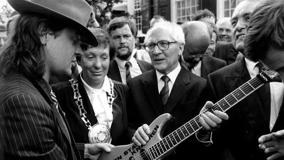 Udo Lindenberg überreicht Erich Honecker eine Gitarre mit der Aufschrift: "Gitarren statt Knarren". | picture-alliance / dpa, Franz-Peter Tschauner SED-Generalsekretär Erich Honecker erhält 1987 in Wuppertal von Udo Lindenberg eine Gitarre mit der Aufschrift: "Gitarren statt Knarren".