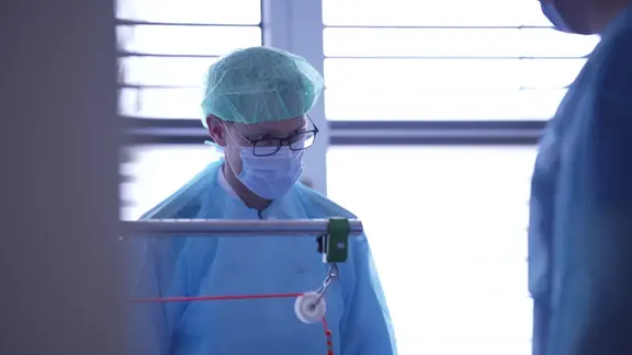 Ein Arzt steht in Kittel, mit OP-Haube und Maske in einem Krankenhaus.