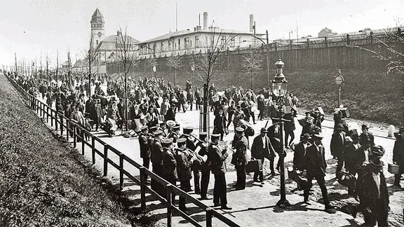 Auswanderer marschieren Anfang des 20. Jahrhunderts von Auswandererlager Ballinstadt in Hamburg zum Hafen. | BallinStadt Auswanderermuseum Hamburg, BallinStadt Auswanderermuseum Hamburg Auswanderer marschieren Anfang des 20. Jahrhunderts von Auswandererlager Ballinstadt in Hamburg zum Hafen.