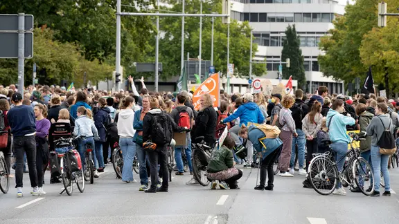Teilnehmer einer Demo stehen und hocken auf einer Straße. | picture alliance/Geisler-Fotopress, Patrick Graf/Geisler-Fotopress Teilnehmer einer Demo stehen und hocken auf einer Straße.