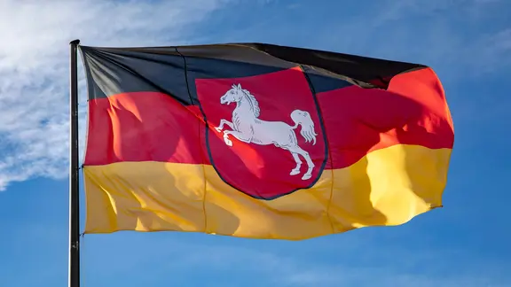 Die Flagge des Bundeslandes Niedersachsen mit Niedersachsenross weht vor blauem Himmel. | picture alliance/Geisler-Fotopress, Robert Schmiegelt Die Flagge des Bundeslandes Niedersachsen mit Niedersachsenross weht vor blauem Himmel.