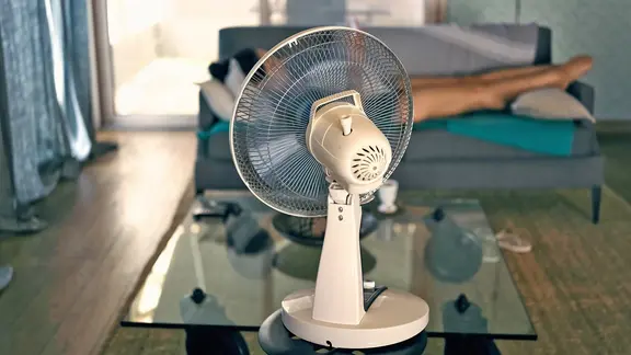 Eine Frau liegt auf einem Sofa vor einem Ventilator. | picture alliance / Hans Lucas | Mathieu Thomasset Eine Frau liegt auf einem Sofa vor einem Ventilator.