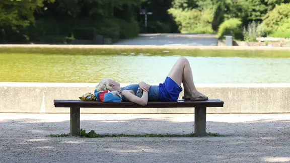 Eine Frau liegt im Schatten auf einer Bank im Hamburger Stadtpark. | Imago, Hanno Bode Eine Frau liegt im Schatten auf einer Bank im Hamburger Stadtpark.
