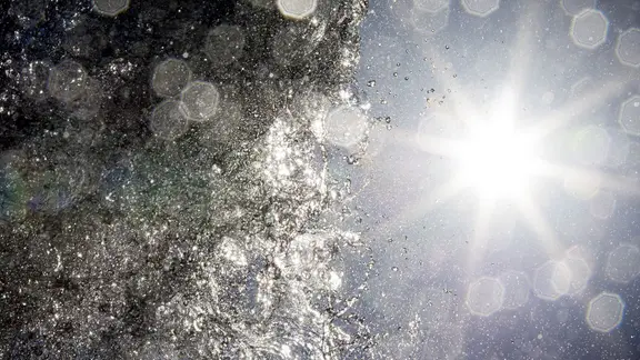 Die Sonne scheint bei hochsommerlichem Wetter hinter dem Klaus-Bahlsen-Brunnen auf dem Platz der Menschenrechte in Hannover.