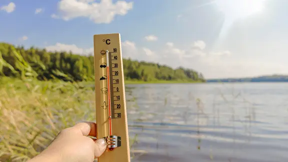 Eine Hand hält ein Thermometer, das mehr als 30 Grad anzeigt. Im Hintergrund ein See. | panthermedia Eine Hand hält ein Thermometer, das mehr als 30 Grad anzeigt. Im Hintergrund ein See.