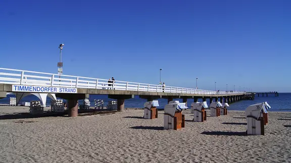 Blick auf die Seebrücke in Timmendorfer Strand . Am Strand stehen mehrere Strandkörbe.