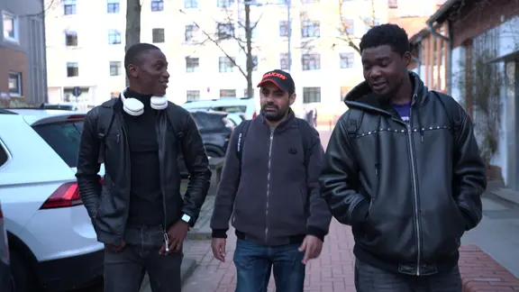 Drei Menschen laufen entlang einer Straße. | NDR Drei Menschen laufen entlang einer Straße.