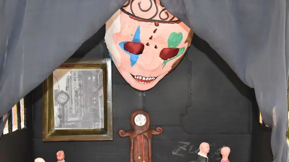 Zu ihrem 35-jährigen Bestehen, zeigt die Jugendkunstschule Magdeburg Porträts und Skulpturen ihrer Schüler. | MDR / Marieke Wuske Ein Kunstwerk von den Teilnehmenden der Jugendkunstschule: kleine Pappmaché-Figuren stehen in einem Karton - wie in einem Puppenhaus. Von der Decke guckt eine riesige, gruslige Maske herunter