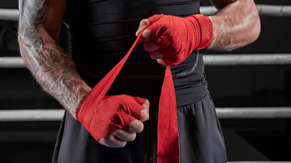 Ein Kickboxer bindet sich im Ring rote Bandagen an die Hände. | picture alliance/imageBROKER, Andy Gin Ein Kickboxer bindet sich im Ring rote Bandagen an die Hände.