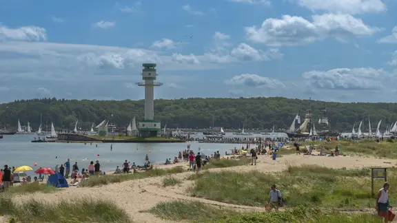 Zuschauer stehen entlang der Kieler Förde und schauen bei der Windjammerparade zu. | picture alliance/imageBROKER | Wolfgang Diederich Zuschauer stehen entlang der Kieler Förde und schauen bei der Windjammerparade zu.