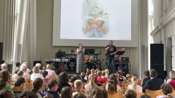 Die Band Seeside präsentierte gemeinsam mit Ulrike Stern vom KND die neue CD im Pommerschen Landesmuseum in Greifswald vor Schülern und Lehrern. | NDR, Christine Senkbeil Auf einer Bühne steht eine Band und eine Sängerin vor Publikum, vor allem Kinder
