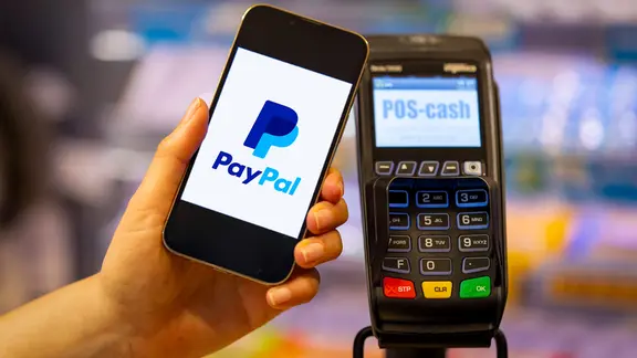 Frau bezahlt mit Smartphone mittels PayPal-App in einem Laden an der Kasse | IMAGO / MiS Frau bezahlt mit Smartphone mittels PayPal-App in einem Laden an der Kasse