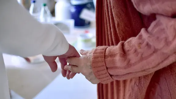 Eine Pflegekraft hält die Hand einer Bewohnerin einer Pflegeeinrichtung. | picture alliance/dpa/dpa-Zentralbild/Britta Pedersen Eine Pflegekraft hält die Hand einer Bewohnerin einer Pflegeeinrichtung.