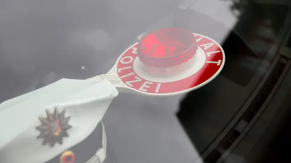Eine Schirmmütze und eine Polizeikelle liegen auf dem Armaturenbrett eines Streifenwagens.