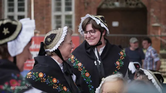 Zwei Frauen in traditionellen Trachten lächeln sich zu. | Screenshot Zwei Frauen in traditionellen Trachten lächeln sich zu.
