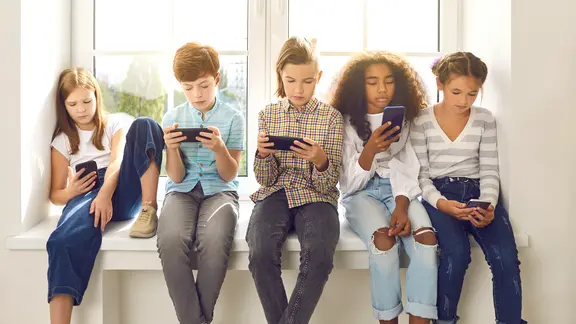 Eine Kindergruppe sitzt auf einer Fensterbank und jeder schaut auf sein Smartphone. | Colourbox, #266241 Eine Kindergruppe sitzt auf einer Fensterbank und jeder schaut auf sein Smartphone.