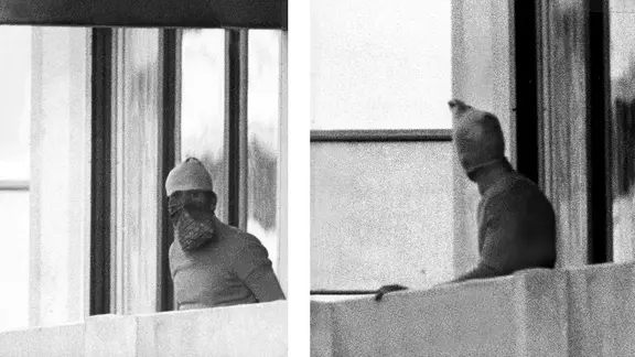 Von dem Attentat der Terrorgruppe "Schwarzer September" im Münchner olympischen Dorf bekommen die Kieler Sportler zunächst nichts mit. | picture-alliance / dpa Zwei der Terroristen während der Olympischen Sommerspiele in München zeigen sich vermummt auf einem Balkon.