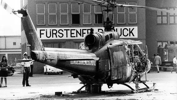Bei der missglückten Befreiungsaktion kommen neun israelische Sportler, ein Polizist und fünf Terroristen ums Leben. | picture alliance / Heinz-Jürgen Göttert, Heinz-Jürgen Göttert Auf dem Militärflughafen Fürstenfeldbruck steht am 6. September 1972 das Wrack eines Hubschraubers vom Bundesgrenzschutz.
