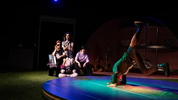 Schauspieler auf der Bühne, drei hocken zusammen und einer macht Breakdance. | Gianmarco Bresadola, Theater Magdeburg Schauspieler auf der Bühne, drei hocken zusammen und einer macht Breakdance.