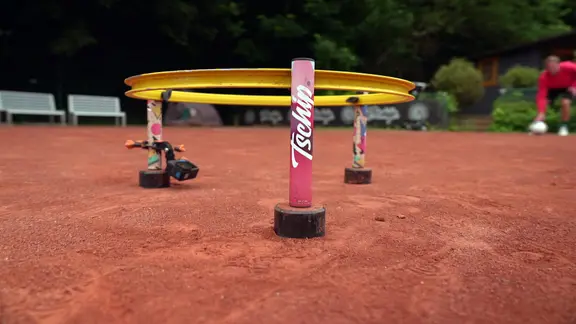 Um diesen Ring dreht sich das Spiel. Er besteht aus einer Fahrradfelge und den eigens entwickelten Füßen. | NDR Ein Tschip-Korb steht auf einem Sportplatz mit rötlichem Sand.