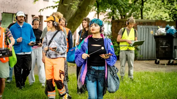 Menschen mit Kopfhörern schlagen mit Klöppeln auf Klinkersteine | Christian Bartsch Menschen mit Kopfhörern schlagen mit Klöppeln auf Klinkersteine