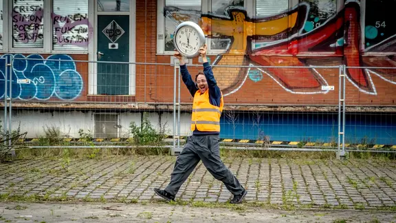 Der Schauspieler Samuel Weiss gibt beim Audiowalk Geschichten aus seiner Kindheit preis. | Christian Bartsch Der Schauspieler Samuel Weiss läuft mit einer großen Uhr vor einer Ziegelwand