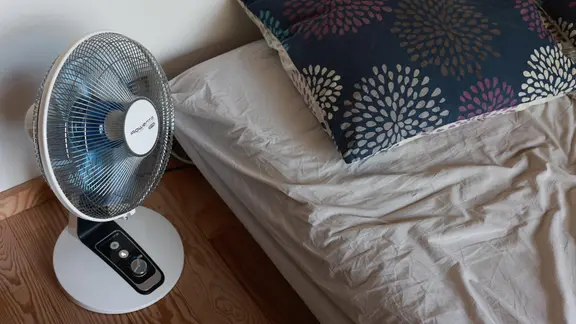 Ein Ventilator steht neben einem Bett.