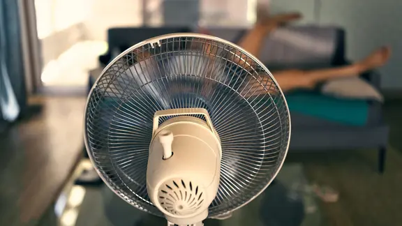 Ein Ventilator ist auf eine auf eine auf dem Sofa liegende Frau gerichtet.