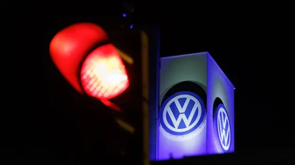 Das Volkswagen-Emblem hinter einer roten Ampel in Osnabrück. | dpa, Friso Gentsch Das Volkswagen-Emblem hinter einer roten Ampel in Osnabrück.