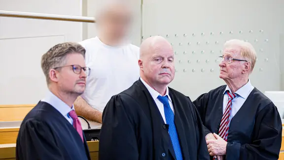 Der angeklagte MHH-Arzt (hinten) steht hinter seinen Verteidigern. | picture alliance/dpa, Moritz Frankenberg Der angeklagte MHH-Arzt (hinten) steht hinter seinen Verteidigern.