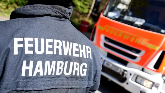 Ein Hamburg Feuerwehrmann und ein Fahrzeug der Feuerwehr. | picture alliance / dpa, Daniel Bockwoldt Ein Hamburg Feuerwehrmann und ein Fahrzeug der Feuerwehr.