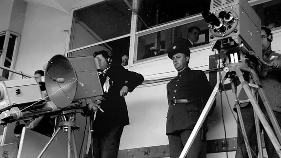 Als erstes Sportereignis überhaupt wird die Fußball-WM 1954 live im Fernsehen in mehrere Länder übertragen. | picture-alliance / dpa , Koll Fernsehkameras beim Endspiel der Fußball-Weltmeisterschaft am 4. Juli 1954 vor im Berner Wankdorf-Stadion. Der Parabolspiegel fängt die akustisch wahrnehmbaren Emotionen der Zuschauer ein und garantiert so den Begleitton der Bildübertragung.