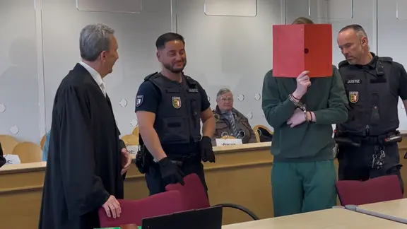 Eine Person im Gerichtssaal verdeckt ihr Gesicht mit einem Ordner | NDR, Sven Jachmann Eine Person im Gerichtssaal verdeckt ihr Gesicht mit einem Ordner
