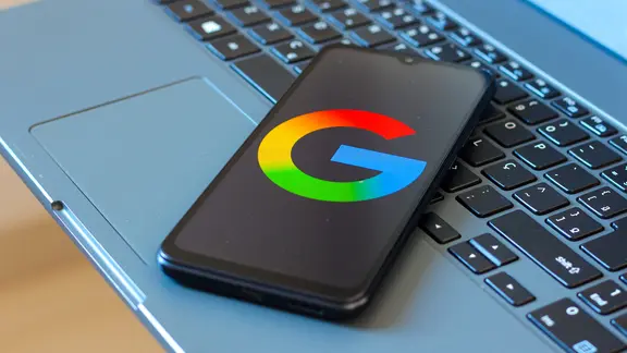 Ein Handy liegt auf einer Laptoptastatur. Das Display zeigt das Google Logo