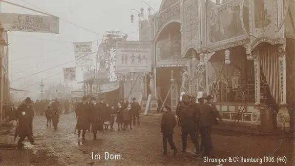 Ein historisches Bild vom Hamburger Dom 1906, Menschen in Winterkleidung gehen an Ständen entlang. | Hamburger DOM Ein historisches Bild vom Hamburger Dom 1906, Menschen in Winterkleidung gehen an Ständen entlang.